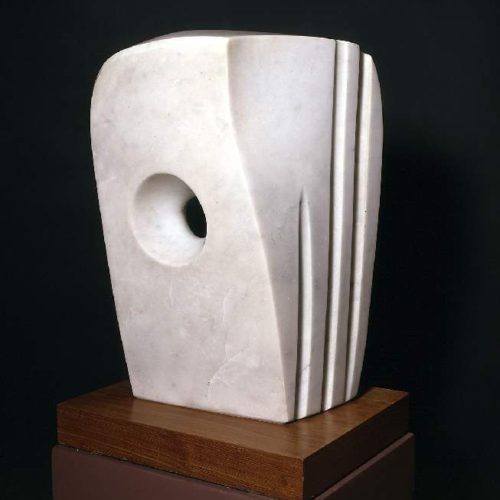 A photograph of a sculpture called Minoan Head made by Barbara Hepworth. It is a tall white marble abstract sculpture with a hole in the middle, going all the way through. The shape is like a cuboid in shape, with rounded edges. The right side has three lines carved into it, perpendicular coming down.