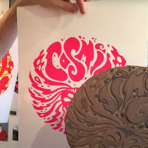Artist Ollie St. Clair is on the left, holding up a print he has made on white paper using pink ink. He also holds up the lino he carved to make the print.